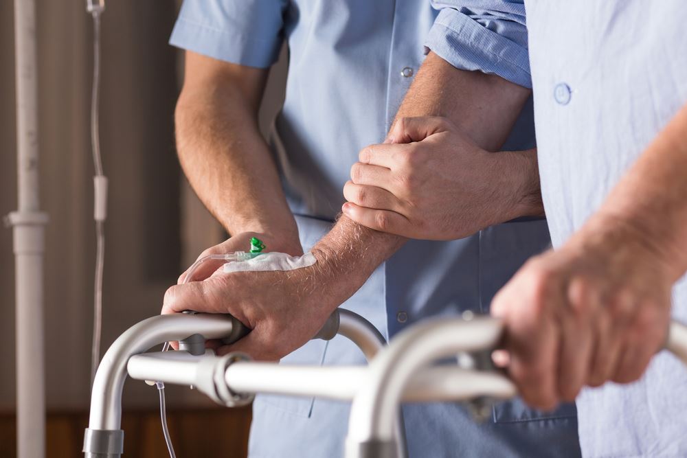 A compassionate nurse gently holds a patient's hand while assisting them in walking, showcasing care and support.